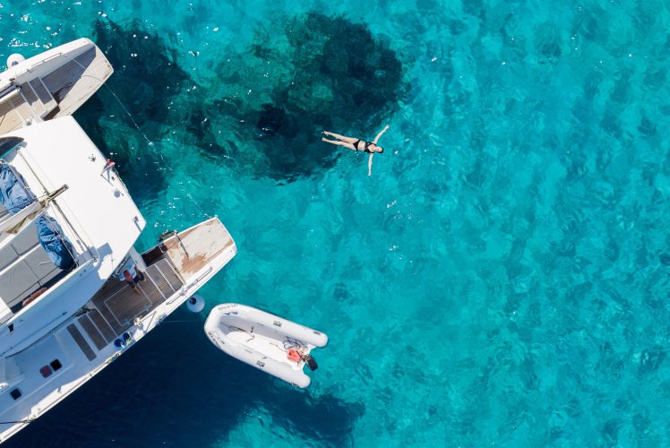 Vue du ciel d'une baigneuse dans l'eau turquoise à côté d'un catamaran et de son annexe